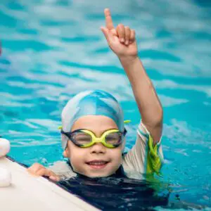 image of child swimming in aqua colored pool with hand up in the air and one finger up.