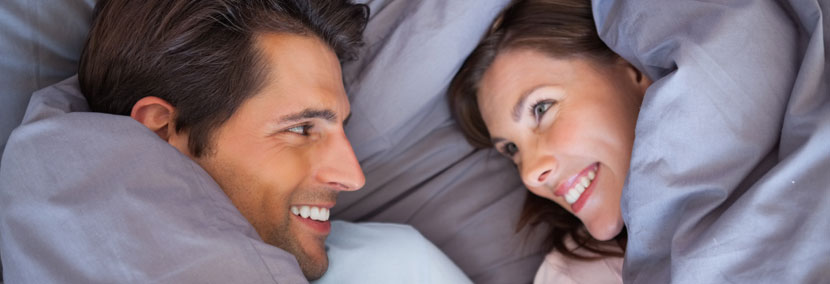 image of happy couple smiling at each other under bed covers