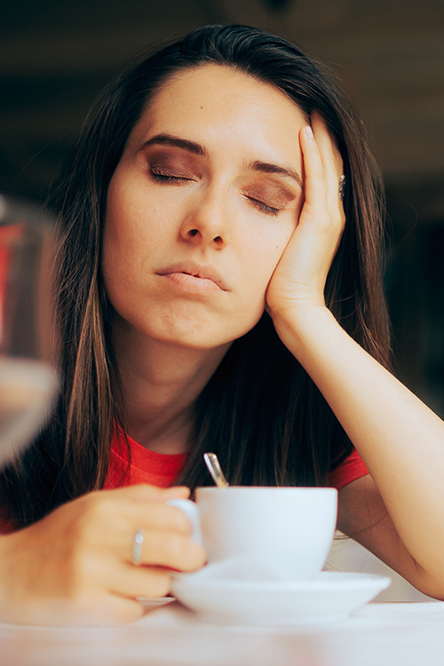 Tired woman half asleep drinking a cup of coffee