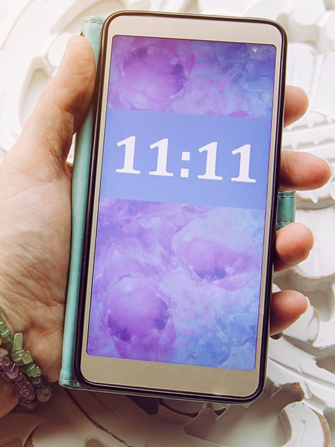 a hand holding a mobile phone with the number 11:11 representing angel numbers