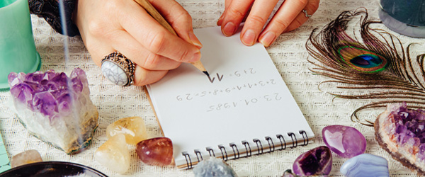Psychic writing email reading notes on a notepad on a table covered with psychic tools including crystals, sage stick and peacock feather