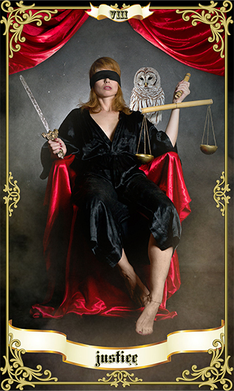 red haired woman blindfolded wearing black garment and holding scales and sword representing justice