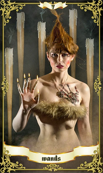 Five of Wands tarot card featuring a pale woman with flame-like red hair standing before tall burning candles, one hand raised with lit fingertips, wearing feathered styling and mystical jewellery inside an ornate gold vintage frame.